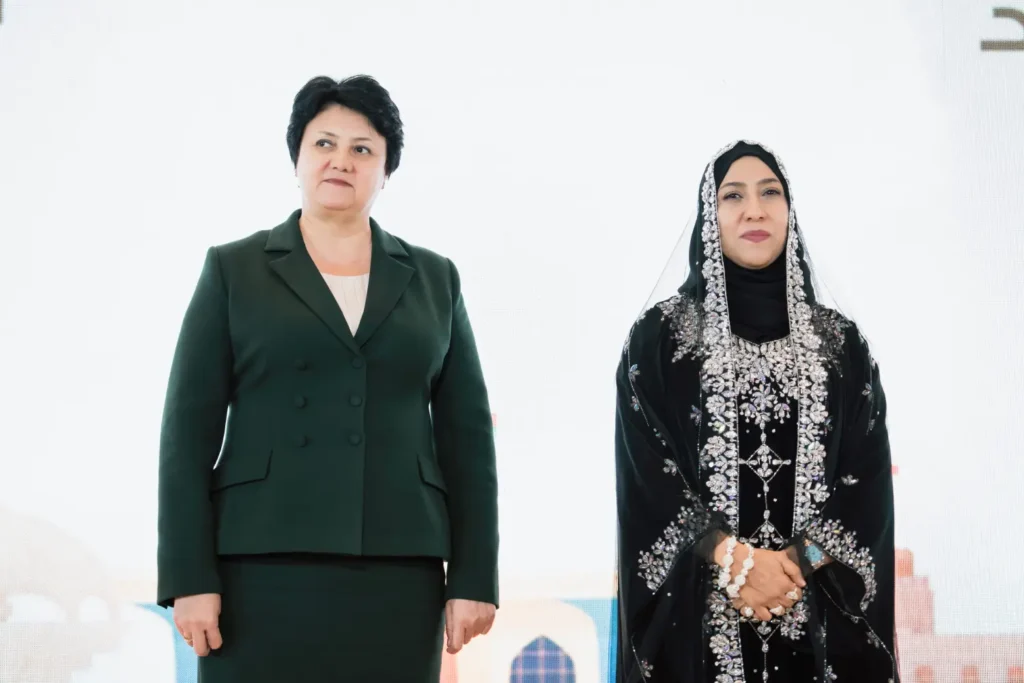 Two women standing side by side: one in a formal dark suit, the other in traditional Omani attire with ornate embroidery