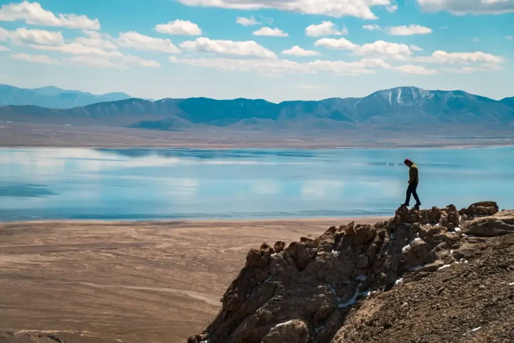 Одинокий человек на скале, вид на озеро и горы