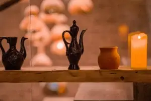 Черные кувшины, кофейник, глиняный сосуд и свеча на деревянной полке