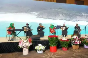 Omani musical ensemble on stage: performers in traditional attire play national instruments against a panoramic view of the sea