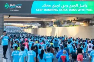 Участники забега Dubai Run в голубых футболках на старте, над ними баннер с надписью „Keep Running. Dubai Runs With You“