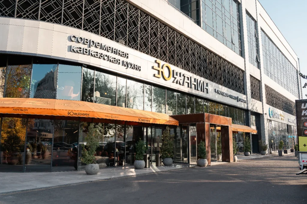 Фасад ресторана «Южанин» с надписью «Современная кавказская кухня», большими стеклянными окнами, декоративными решётками и оранжевым навесом