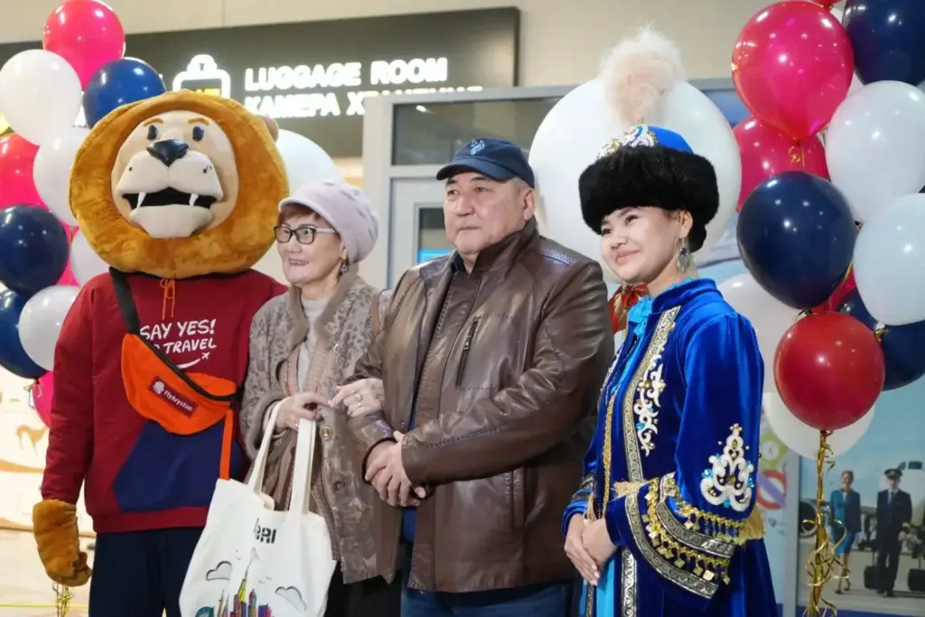 A group of a lion mascot, an elderly couple, and a woman in traditional attire in front of the «Luggage Room» sign