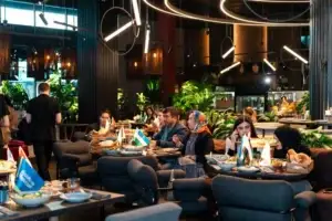 Гости ресторана наслаждаются трапезой в современном интерьере с обилием зелёных растений и стильными круглыми светильниками