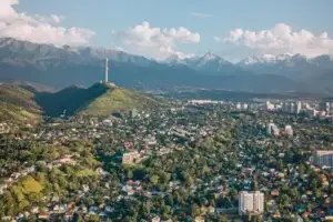A park with numerous trees and residential buildings, with a TV tower rising above it on a hill