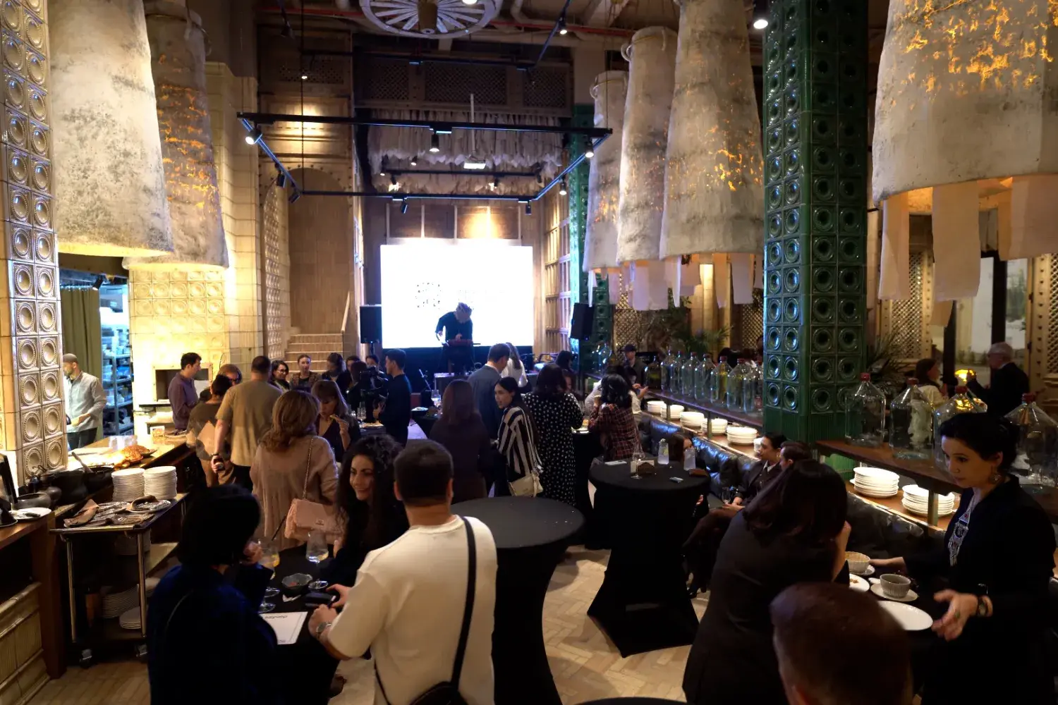 Гости общаются в ресторане в стиле лофт, на заднем плане — сцена с экраном