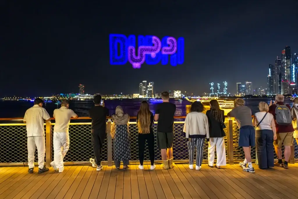 People crowded on the bridge, watching and filming a light show in which glowing drones flock to the word Dubai in the night sky