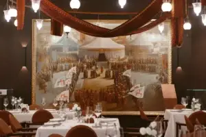 Ресторанный зал с картиной «Пленение Шамиля» Теодора Горшельта на стене. Сервированные столы, текстильные драпировки, подвесные светильники