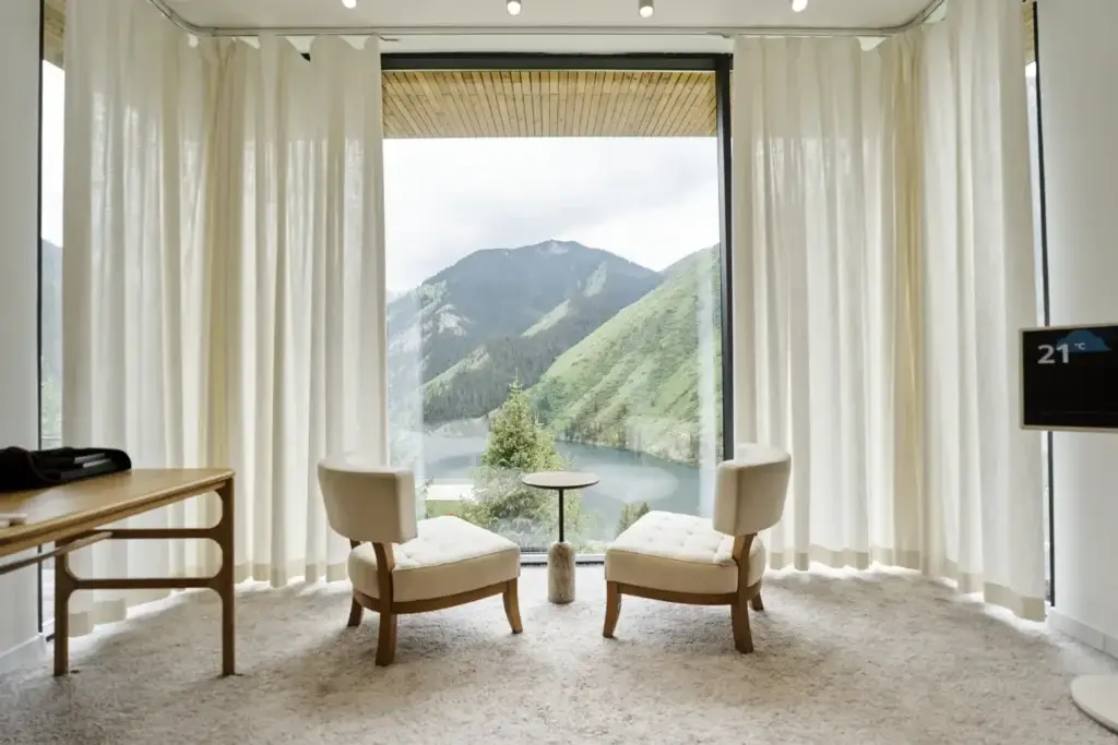 Interior of a guest room with a panoramic window overlooking mountains and a lake in a nature-based hotel in Kazakhstan