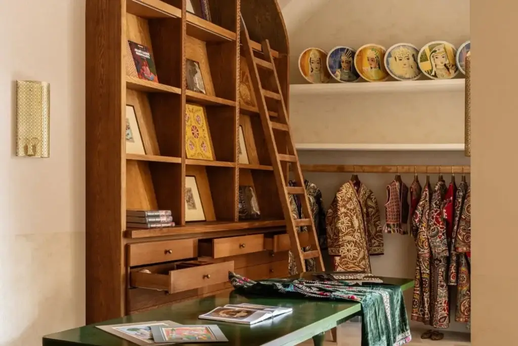 A wooden arched shelf, a green tabletop, a ladder, ethnic costumes hanging on a rack, and painted plates on the wall