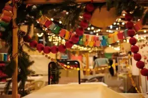 Colorful paper chain garlands and red ornaments under pine branches at a festive holiday market with warm string lights