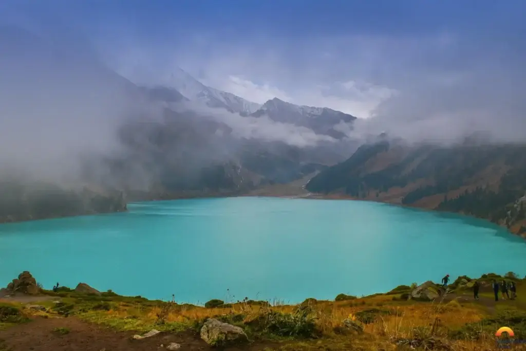 Big Almaty Lake with turquoise water surrounded by mountains and low clouds
