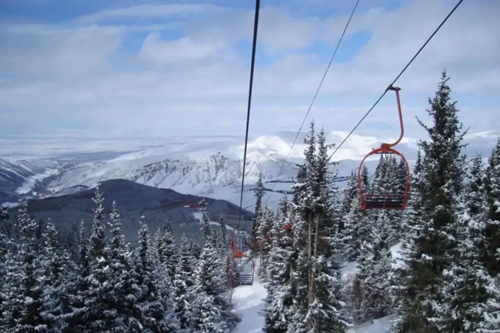 A chairlift amid snow-covered firs with a view of mountain ranges
