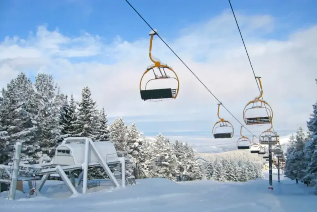 Chairlift at a ski resort, snow-covered firs, clear blue sky