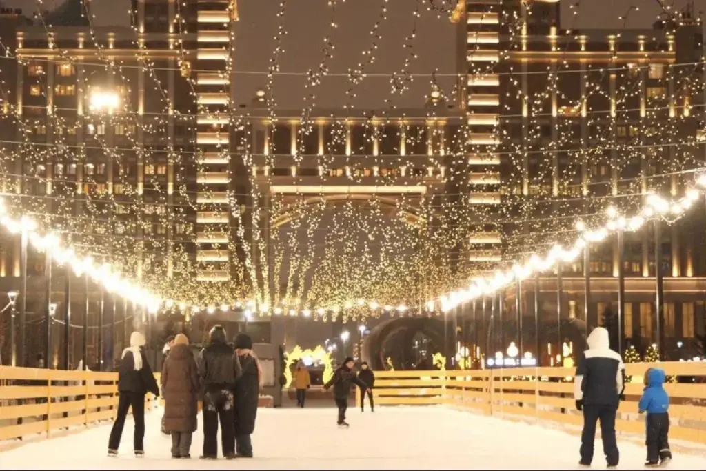 Люди катаются на коньках на уличном катке в Астане, украшенном праздничной гирляндой