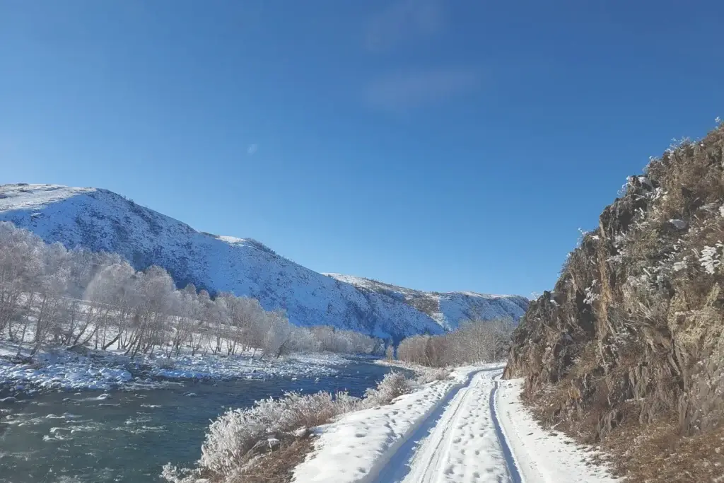 Фото заледеневшей реки Бухтарма у села Мойылды и пролегающая рядом покрытая сугробами снега дорога на пасеку