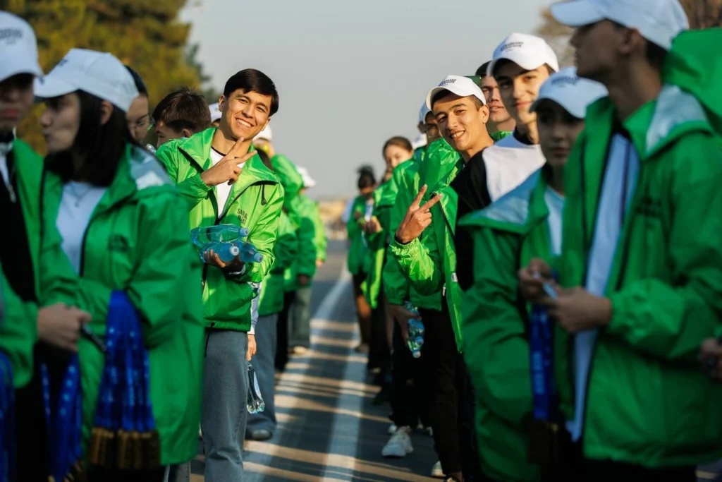 A group of young people in green windbreakers and white caps posing on the street, some showing victory signs