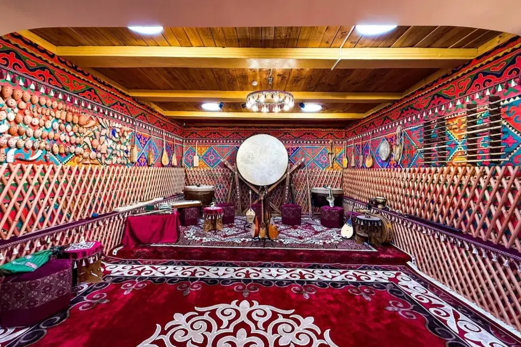 Interior of a traditional yurt with national musical instruments, patterned carpets, and a wooden ceiling