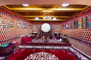 Interior of a traditional yurt with national musical instruments, patterned carpets, and a wooden ceiling