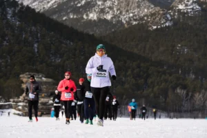 Runners participate in a winter race on a snow-covered course with mountains in the background.