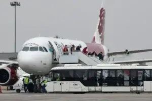 Passengers disembark from an aircraft via a mobile staircase on the airport apron