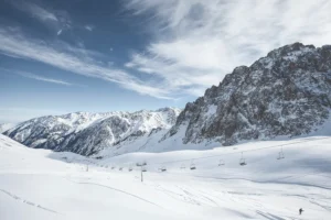 Snow-covered mountain slopes with ski lifts and a cable line against rocky peaks and a clear sky