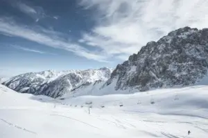 Заснеженные горные склоны с подъемниками и канатнои дорогои на фоне скал и ясного неба