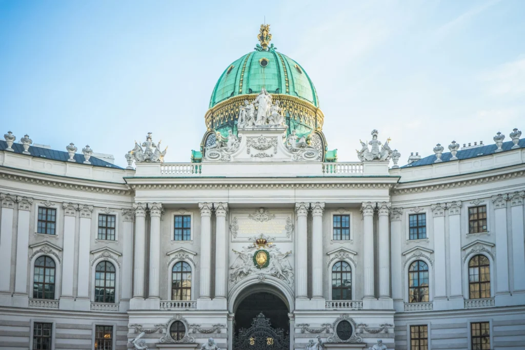 Facade of a historic palace with columns and a green domed roof adorned with sculptures and ornate details