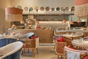 Middle Eastern inspired restaurant interior with an open kitchen, copper pendant lights, and set dining tables