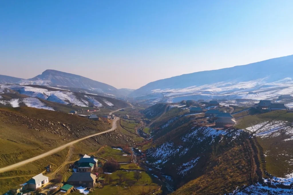 Mountainous terrain viewed from above, with houses and snow-covered peaks