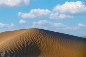 A large sand dune under a blue sky with white clouds in the desert in Uzbekistan