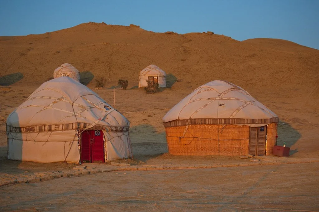 A camp of three traditional yurts in a dry desert landscape against the backdrop of a large sandy hill