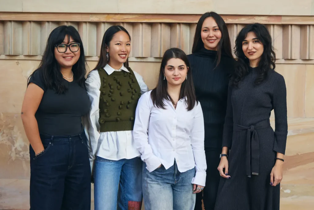 Group of women standing together indoors, dressed in dark formal attire, posing for a group photo.